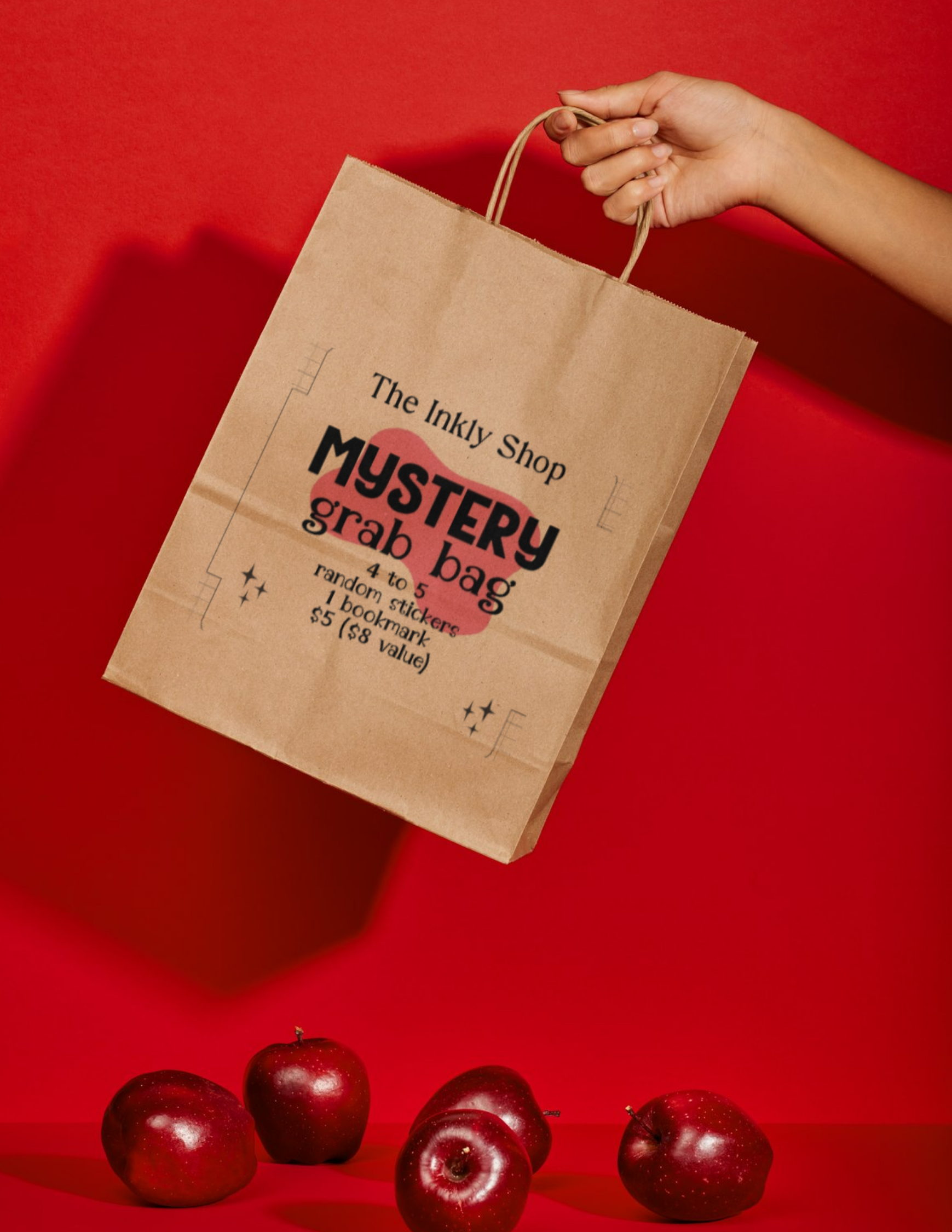 The Inkly Shop Mystery Grab Bag — kraft paper bag held up against a red background with apples