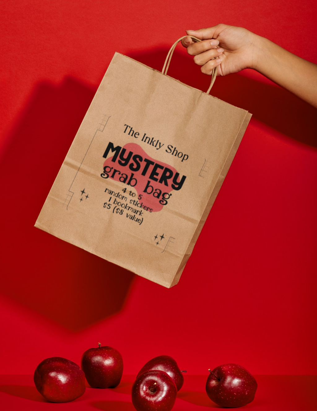 The Inkly Shop Mystery Grab Bag — kraft paper bag held up against a red background with apples